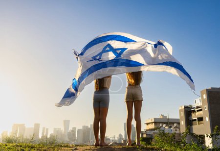 Dos chicas ondeando la bandera de Israel como Cúpula de Hierro. Miran el horizonte de Givatayim. Yom Haatzmaut o Stand with Israel concepto