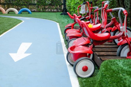 Rote Dreiräder reihen sich neben einem Parcours auf einem Kinderspielplatz