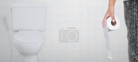 Photo for A person suffering from diarrhea holds a roll of toilet paper in front of the toilet bowl - Royalty Free Image