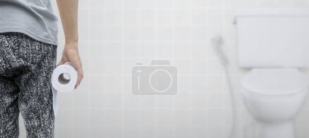 Photo for A person suffering from diarrhea holds a roll of toilet paper in front of the toilet bowl - Royalty Free Image