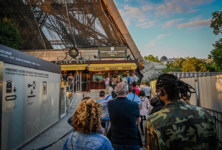 Foto de París, Francia, 1 de julio de 2022. Gente haciendo cola para comprar entradas y acceder a la Torre Eiffel. La cálida luz de la tarde lo ilumina completamente. - Imagen libre de derechos