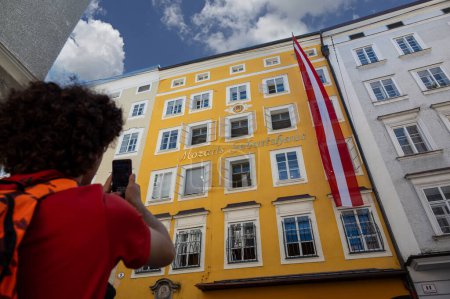 Salzburg, Austria, August 15, 2022. A cute boy is photographing mozart's house with his cellphone as a souvenir of the holiday. Technology use concept.