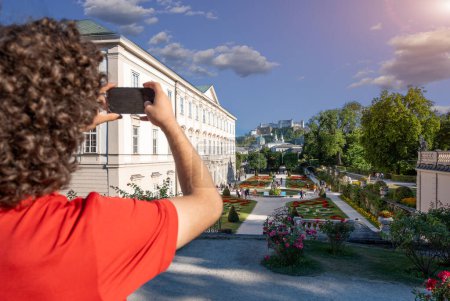 Salzburg, Österreich, 15. August 2022. Nahaufnahme eines jungen Mannes, der den Garten von Schloss Mirabell tagsüber fotografiert. Die Menschen besuchen sie und erkunden sie. Die Festung Hohensalzburg im Hintergrund.