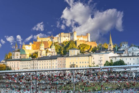 Salzburg, Österreich, 15. August 2022. Konzeptbild der Liebesbrücke mit Vorhängeschlössern im Vordergrund und der Altstadt mit Hügel und Festung im Hintergrund. Goldene Stunde.