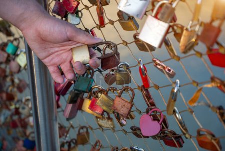 Salzburg, Austria, August 15, 2022. Close-up on the hand of a Caucasian young man holding one of the padlocks on the bridge of love. Conceptual image.