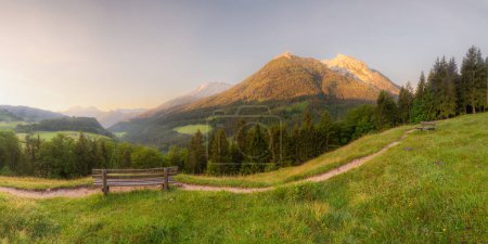 Pradera con carretera y banco cerca del lago Hintersee al atardecer en el Parque Nacional Berchtesgaden, Alpes bávaros superiores, Alemania, Europa. Recorte de camino del cielo