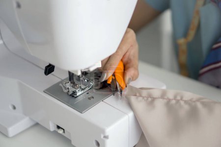 Photo for Closeup dressmaker hand cut the thread with scissors after finish sewing on a machine. - Royalty Free Image
