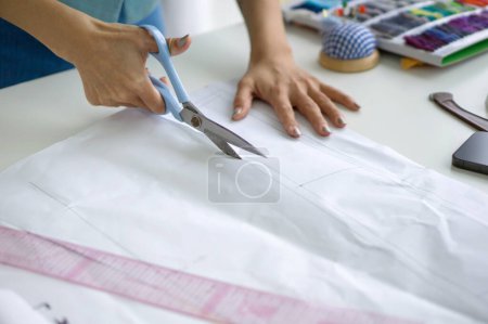 Foto de Closeup dressmaker mano utilizar tijeras para cortar patrón de papel de boceto. - Imagen libre de derechos