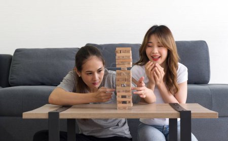 Téléchargez les photos : Deux femmes asiatiques aiment jouer jeu de blocs en bois dans le salon. Les joueurs prennent tour à tour enlever un bloc à la fois d'une tour construite de 54 blocs. - en image libre de droit
