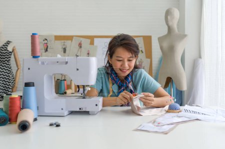 Téléchargez les photos : Young dressmaker cut the thread with scissors after finish sewing on a machine. Asian woman working in home base cloth design business. - en image libre de droit