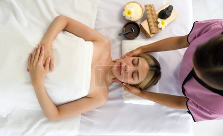 Eine ruhige Wellness-Szene mit einer entspannten Frau, die auf einem Massagetisch liegt, einem ausgebildeten Profi, der beruhigende Technik auf ihr Gesicht anwendet.
