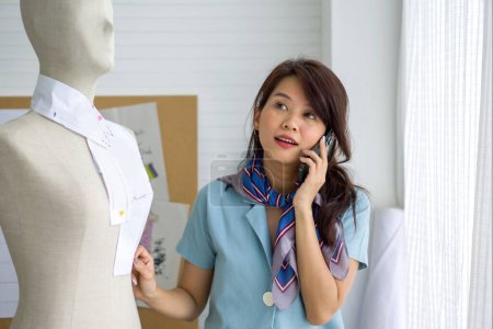 Photo for Young asian woman engaging in a phone conversation while standing beside a life-sized mannequin. - Royalty Free Image
