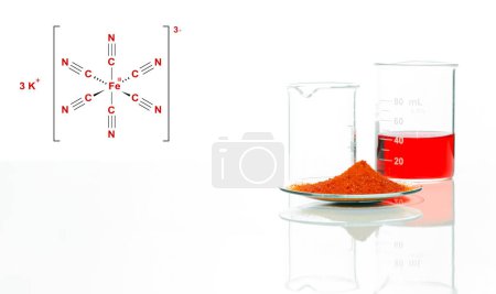Foto de Ferricianuro de potasio en reloj químico Lugar del vidrio junto a la sustancia química líquida roja en el vaso de precipitados en la mesa blanca del laboratorio, con el laitmotif complejo de una estructura química compuesta. - Imagen libre de derechos
