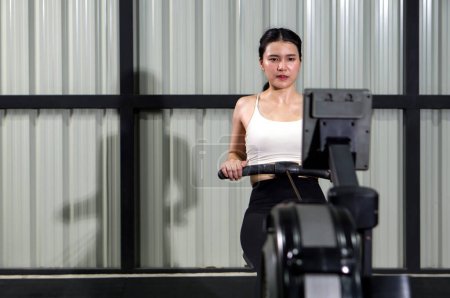 Photo for Health and active lifestyle concept. An athletic woman in sportswear is engaged in an intense workout session on a rowing machine inside a well-equipped gym. - Royalty Free Image
