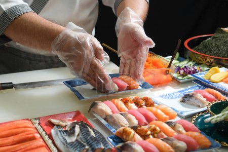Téléchargez les photos : Un chef habile prépare une variété de sushis sur une table. Mélangeant saveur, texture et couleur, le chef crée de l'art culinaire. Chaque sushi est un chef-d'œuvre précis, mettant en valeur leur expertise et leur dévouement. - en image libre de droit