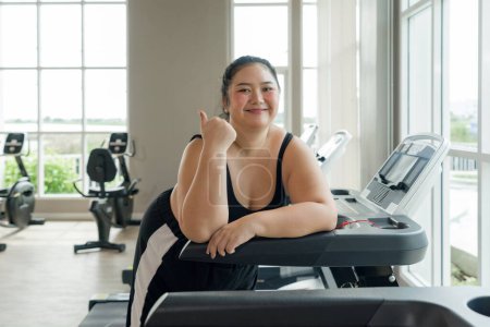 Photo for A plus-size woman stand on a gym treadmill, resting or preparing to exercise. - Royalty Free Image