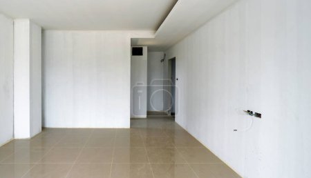 Photo for A bare white Primer color painted wall room with shiny marble tiled floor and lots of empty space. Unfinished room. Door, service access panel and electrical outlet have not yet been installed. - Royalty Free Image