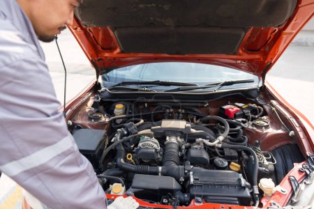 Foto de Un mecánico en uniforme y guante protector mira el motor de un coche deportivo para arreglarlo. Ambiente de trabajo en taller de reparación de automóviles. - Imagen libre de derechos