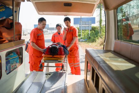 Grupo de paramédicos o técnicos médicos de emergencia (EMT) en uniforme naranja coloca a una víctima de un accidente de cuello y cabeza en una cama en una ambulancia. Asistencia urgente durante el accidente de tráfico.