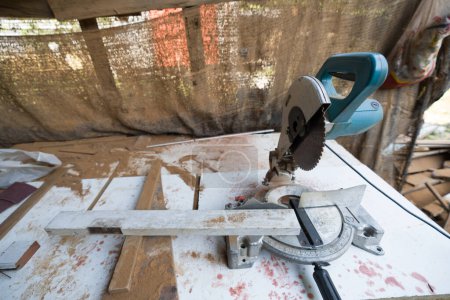 A compound miter saw placed on a work table with wood shaving and typical construction debris around it. 