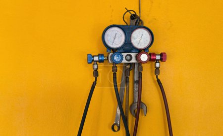 Manifold Gauge with hoses and a wrench on a yellow wall.