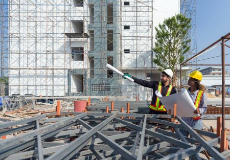 A construction site with engineers and architect, discussing the progress of the building under construction. Both wearing hardhat and safety vest. Pile of steel structure are in the foreground.