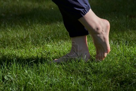 Téléchargez les photos : Image de pieds femelles nus debout sur de l'herbe fraîche humide un pied levé faisant une vue d'un côté - en image libre de droit