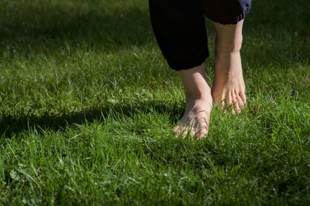 Téléchargez les photos : Image de pieds femelles nus debout sur de l'herbe fraîche humide un pied levé faisant une vue de face étape - en image libre de droit