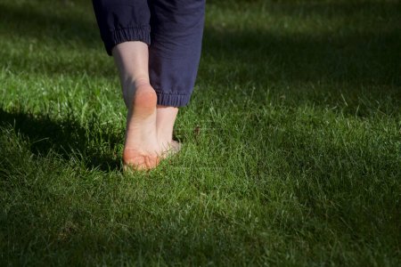 Téléchargez les photos : Image de pieds femelles nus debout sur de l'herbe fraîche humide un pied levé rendant visible une semelle de marche - en image libre de droit