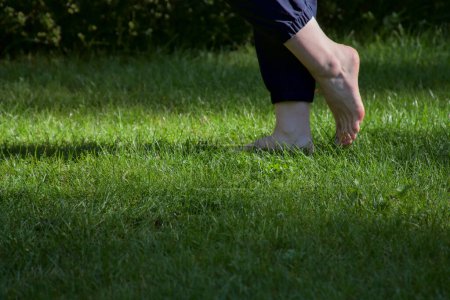 Téléchargez les photos : Image de pieds femelles nus debout sur de l'herbe fraîche humide un pied levé faisant une vue de côté étape - en image libre de droit