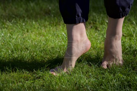 Téléchargez les photos : Image de pieds femelles nus debout sur de l'herbe fraîche humide faisant un pas en avant sur les orteils gros plan - en image libre de droit