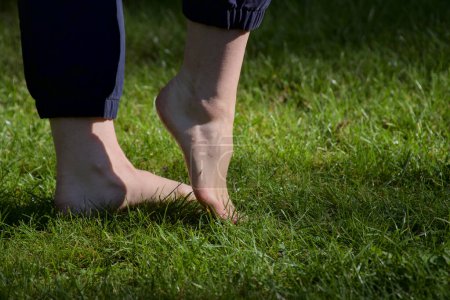 Téléchargez les photos : Image de pieds femelles nus debout sur de l'herbe fraîche humide faisant un pas vers l'avant vue de côté gros plan - en image libre de droit