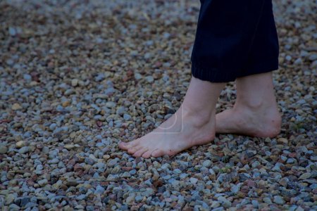 Téléchargez les photos : Image de pieds féminins nus debout sur de petites pierres acérées faisant un pas - en image libre de droit