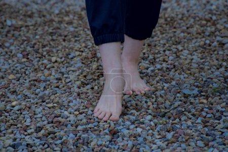 Téléchargez les photos : Image de pieds femelles nus debout sur de petites pierres acérées un pied à moitié levé vue de face - en image libre de droit