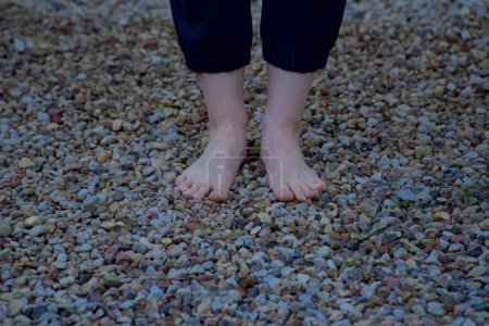 Téléchargez les photos : Image de pieds femelles nus debout sur de petites pierres acérées vue de face - en image libre de droit