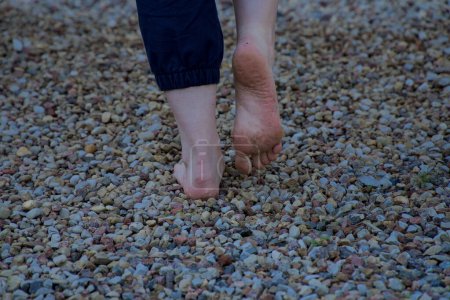 Téléchargez les photos : Image de pieds femelles nus debout sur de petites pierres acérées un pied semelle sale à moitié soulevée vue arrière - en image libre de droit
