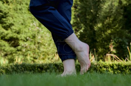 Téléchargez les photos : Image de pieds femelles nus debout sur de l'herbe fraîche humide faisant un pas vers l'avant vue latérale - en image libre de droit