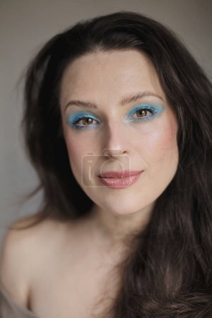 Téléchargez les photos : Portrait d'une femme portant un fard à paupières bleu clair brillant et ses cheveux foncés ondulés vers le bas - en image libre de droit