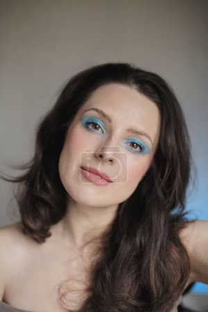 Téléchargez les photos : Portrait d'une femme portant un fard à paupières bleu clair brillant et ses cheveux foncés ondulés vers le bas - en image libre de droit