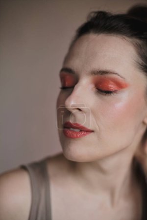 Téléchargez les photos : Portrait d'une femme aux yeux fermés portant un maquillage extraordinaire avec des fards à paupières rouges et du rouge à lèvres rouge, les cheveux attachés - en image libre de droit