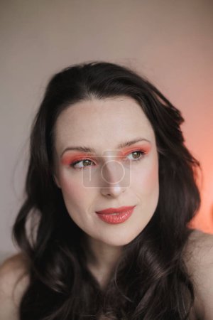 Portrait of a young woman wearing makeup in red and peach tones with her dark hair down