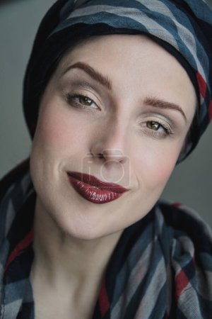 Close up portrait of a woman wearing dark bold lipgloss contrasting with pale skin and a shawl around her head