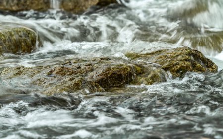 Schneller Quellfluss, der über Felsen fließt und Wildwasserwellen bildet, Detailaufnahme - abstrakter Naturhintergrund.