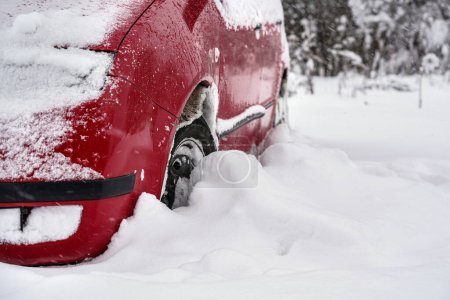 Rotes Auto nach starkem Schneesturm in tiefer Schneeschicht geparkt, Detail zum Reifen - nur halbe Felge sichtbar.