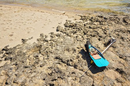 Esnórquel, máscara, aletas y arpón de pesca con lanzas simple en la playa rocosa iluminada por el sol cerca del mar, equipo pesquero malgache local.