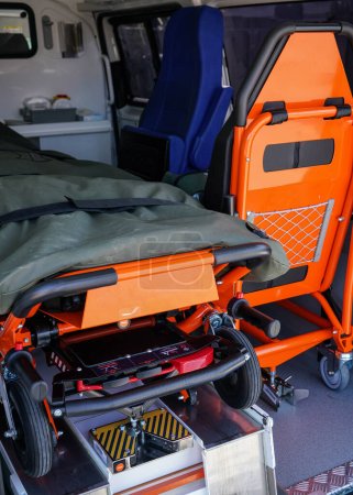 Parte posterior del vehículo de ambulancia, camilla de transporte naranja brillante y silla de paciente visible