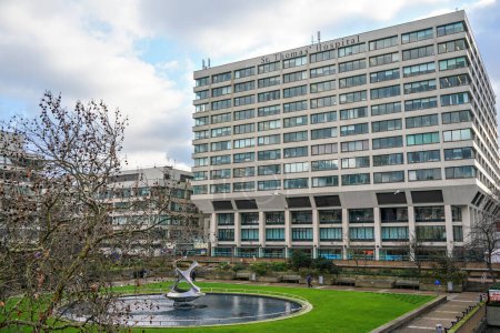 Photo for London, United Kingdom - February 02, 2019: St Thomas hospital building wall near London Bridge, green lawn with fountain in foreground. It is academic health science centre and teaching hospital - Royalty Free Image
