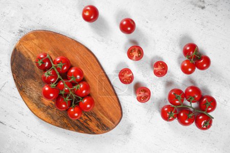 Téléchargez les photos : Petites tomates rouges vibrantes avec des vignes vertes sur planche à découper en bois, table en pierre blanche sous, vue d'en haut - en image libre de droit