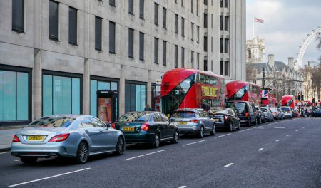 Téléchargez les photos : Londres, Royaume-Uni - 02 février 2019 : Route de rue Victoria plutôt vide, bus rouges et voitures en attente sur le côté, drapeau britannique sur le bâtiment près de l'œil de Londres en arrière-plan - en image libre de droit