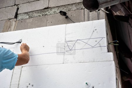 Téléchargez les photos : Travailleur installant l'isolation thermique de polystyrène sur les murs nus de la maison, détail aux mains marquant des panneaux de mousse blanche - en image libre de droit